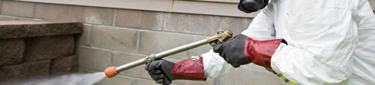Pest control technician applying exterior insect treatment along a home foundation in Saint Louis, MO