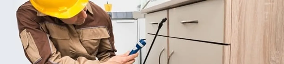 Roach exterminator applying treatment under kitchen cabinets in Saint Louis, MO
