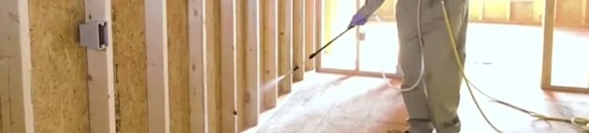Termite treatment technician applying spray along framing and unfinished walls in Saint Louis, MO